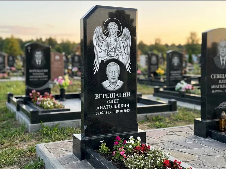 Памятник с гравировкой иконы: стела с резным навершием и нимбом в золоте — гравировка образа Спасителя, высокие разросшиеся туи полукругом, работа «Мельникова» в Ростове-на-Дону